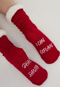 Czerwone skarpety z białymi, puszystymi mankietami. Napis na jednej skarpecie brzmi "DROGI MIKOŁAJU", a na drugiej "MOGĘ TO WYJAŚNIĆ". Dzianinowa faktura.