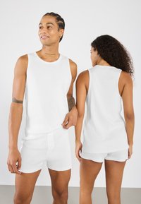 Vita ribbade linnen och shorts med sömlösa kanter, mjuk textur och en åtsittande design. Synlig knappdetalj på shortsen.