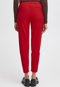 Červené zúžené kalhoty s elastickým pasem a dvěma zadními kapsami, s hladkou texturou a slim fit střihem, který se zužuje u kotníků.