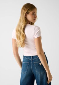 Light pink ribbed short-sleeve top paired with high-waisted blue denim jeans. Jeans feature a triangular logo patch on the back pocket.