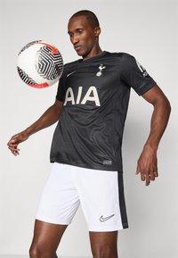 Maglia da football nera con logo "AIA" bianco, marchio Nike e texture geometrica, abbinata a pantaloni bianchi con logo nero.