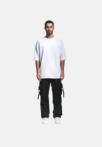 Hvit bomull t-skjorte med avslappet passform, kombinert med svarte cargo-bukser med flere lommer og justerbare snører, brukt med hvite sneakers.
