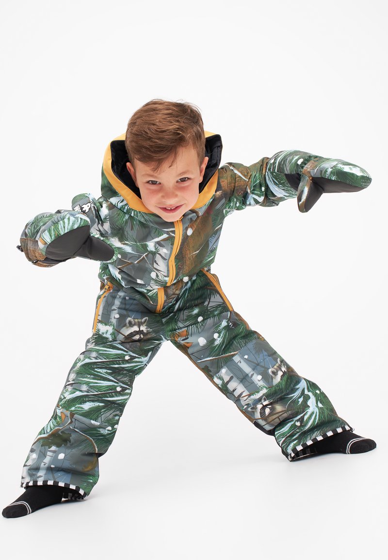 Børns vinteroveralls med et mønster af skov i grøn, brun og hvid, med en gul hætte og sorte vanter, designet til varme og bevægelighed.