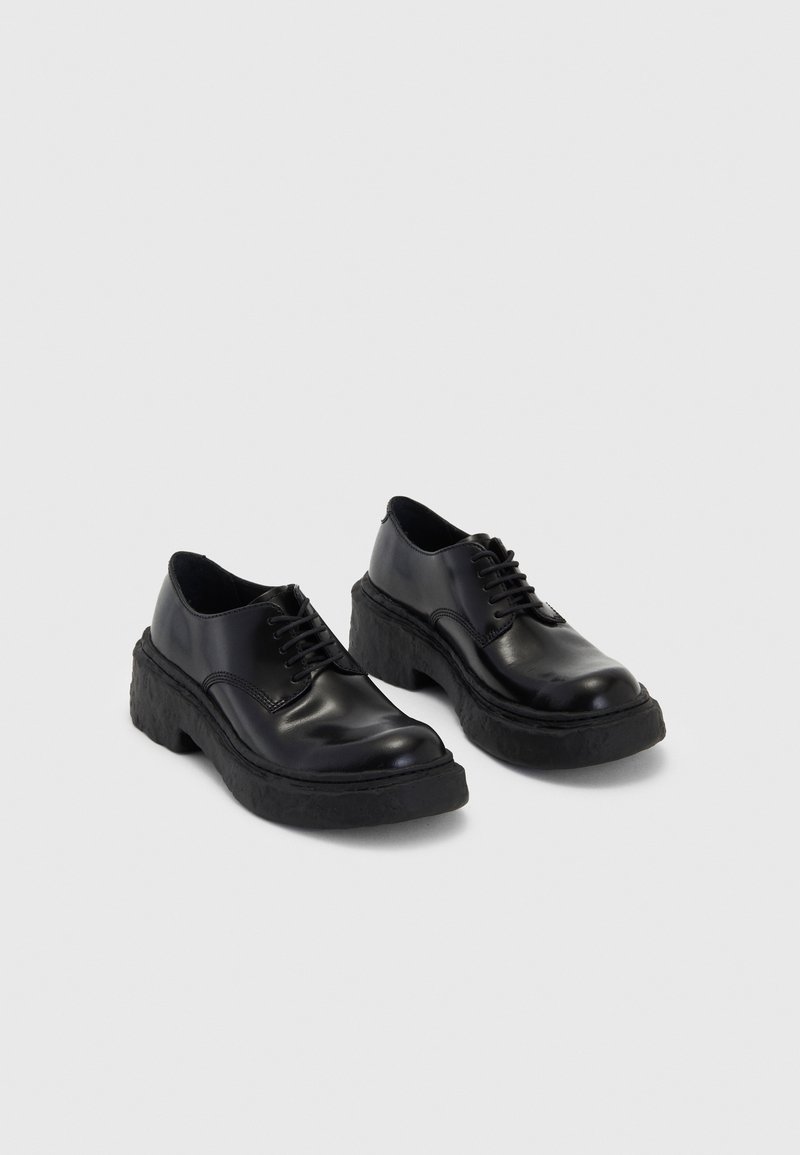 Black leather shoes with a chunky black rubber sole, featuring round toes and a lace-up design. Smooth texture with subtle stitching details.