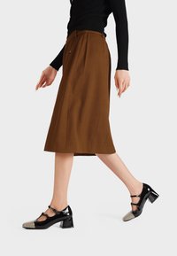 Gonna midi marrone con pieghe laterali, maglione fitted nero e scarpe con tacco nere e metalliche con cinturini alla caviglia e punta quadrata.