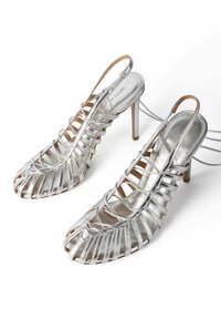 Sandali alto in argento con design open toe, caratterizzati da cinturini incrociati e slingback. Materiale metallico liscio e forma affusolata.