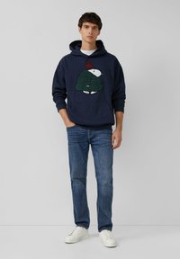 Marine hoodie met een schildpad grafiek, met een gestructureerd ontwerp. Gecombineerd met blauwe spijkerbroek en witte sneakers. Eenvoudige, casual outfit.