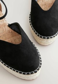 Espadrile negre din suede, cu o decupare în formă de V, talpă din jute în formă de wedge și cusături albe contrastante pe margine. Textură netedă.