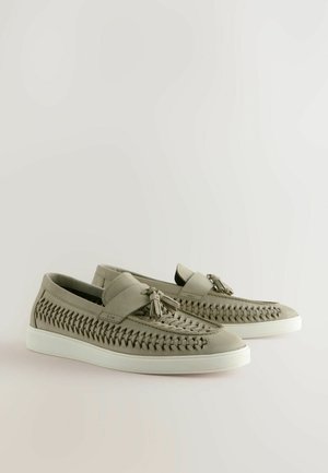 Hellgraue Slippers mit geflochtenen Details, glatter Oberfläche und weißen Gummisohlen. Sie verfügen über einen flachen Riemen und dekorative Quasten.