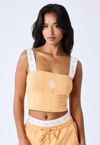 Crop top in zacht oranje stof met witte banden en een logo. Getextureerde patronen en gestikte accenten op de stof.