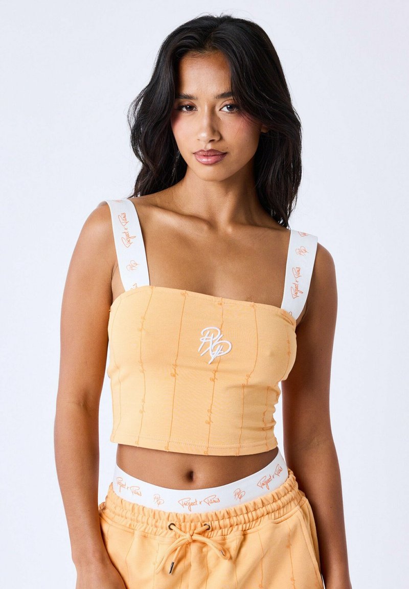 Crop top in zacht oranje stof met witte banden en een logo. Getextureerde patronen en gestikte accenten op de stof.
