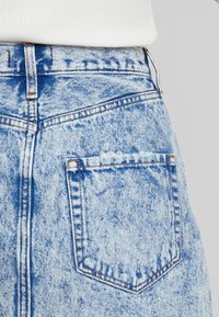 Jeans in denim azzurro chiaro con finitura slavata e testurizzata, caratterizzati da una tasca posteriore e dettagli di cuciture visibili. Design a vita alta.