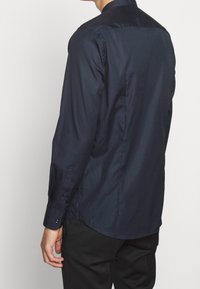 Marineblauw shirt met lange mouwen, een gladde, glanzende textuur, knoopmanchetten en een getailleerd achterkant ontwerp, met een strakke, minimalistische silhouet.