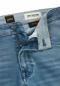 Jeans in denim blu con una texture liscia, dotati di una chiusura con cerniera, cuciture arancioni a contrasto e etichette contrassegnate con "BOSS" e "SOFT MOTION".