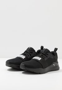 Zwarte sportschoenen met een mesh-structuur, voorzien van een wit logo op de bovenkant. Ronde neus, vetersluiting en een gevoerde kraag voor comfort.
