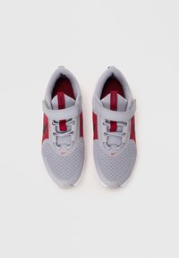 Chaussures de sport grises avec des accents rouges, tige en maille et sangle en tissu, présentant un bout arrondi et une semelle flexible.