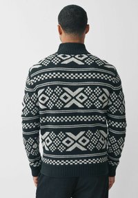 Schwarz-weißer, gemusterter Pullover mit geometrischen Designs und strukturiertem Rippenkragen und -bündchen. Hergestellt aus dickem Strickmaterial.