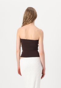 Brun strapless topp med en figursydd design, tillverkad av mjukt tyg. Bärs tillsammans med en texturerad vit kjol, med en snug midja.