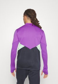 Långärmad sporttopp med en livfull lila övre del och en geometrisk mintgrön och svart nedre sektion. Mjuk textur och åtsittande design.