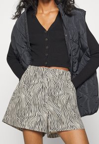 Svart ribbad kofta med små blommor som knappar, kombinerad med beige shorts med ett svart zebramönster och en ofodrad pufferväst.