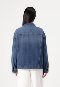 Jeansowa kurtka w średnim odcieniu niebieskiego, w oversize'owym fasonie, z wygiętym kołnierzem, bocznymi kieszeniami i zapinanymi mankietami. Gładka tekstura, brak widocznych wzorów.