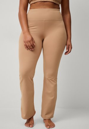 Beige, højtaljede leggings i et glat, strækbart stof. Sløjfedesign med subtile syninger. Barfodede fødder synlige.