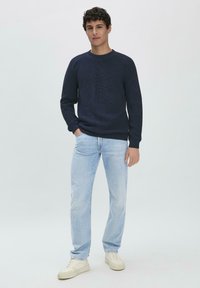 Marineblaues Strickpullover mit Rundhalsausschnitt, kombiniert mit hellblauen Jeans und weißen Sneakern. Lässige Passform, strukturiertes Material und gerippte Bündchen.