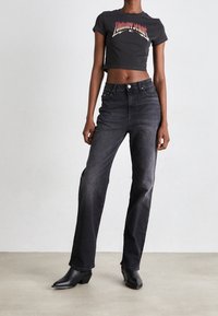 Černé zkrácené tričko s logem "Tommy Jeans", spojené s tmavými džínami s vysokým pasem a černými kotníkovými botami na podpatku.