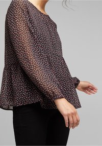 Blusa nera floreale realizzata in chiffon leggero, con una vestibilità comoda, scollatura tonda e maniche lunghe leggermente arricciate con polsini elastici.