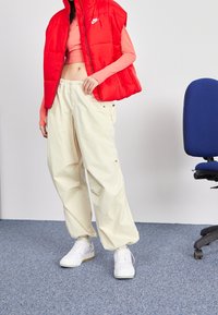 Röd puffväst, ljusrosa långärmad topp och lösa beige byxor. Vita sneakers med en texturerad sula. Avslappnad gatastil.