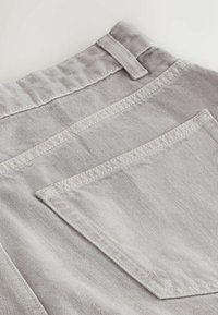 Tissu en denim gris clair avec des coutures détaillées montrant une poche arrière et une boucle de ceinture sur un pantalon ou un short.