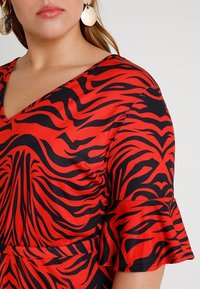 Top con estampado de cebra rojo y negro, con escote en V, mangas cortas acampanadas y textura suave. Presenta un detalle recogido en la cintura.