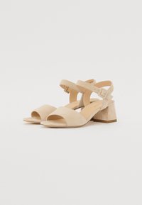 Beige suede heeled sandals feature an open toe, wide front strap, cross ankle straps, and a block heel. Smooth texture with a minimalist design.