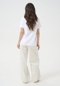 T-shirt en coton blanc à manches courtes, associé à un pantalon ample de couleur crème avec poches. Texture lisse, coupe décontractée.