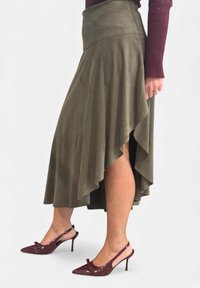 Gonna asimmetrica verde oliva in tessuto morbido con pieghe, abbinata a décolleté slingback lucide color marrone amaranto con dettaglio a fiocco e tacco a stiletto.