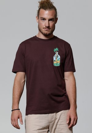 T-shirt en coton bordeaux avec un design graphique représentant une bouteille avec des palmiers et une scène de plage sur le côté gauche de la poitrine. Style simple à col rond.