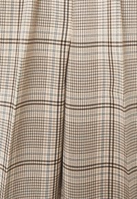 Tissu en tartan marron et beige avec un tissage texturé. Présente un motif en grille avec de fines accents bleus et des épaisseurs de ligne variées.