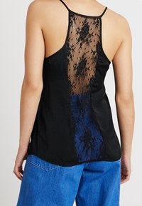 Haut noir sans manches avec un panneau en dentelle à l'arrière, complété par une section bleue unie. Texture lisse avec des bretelles fines.