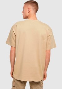 Beige oversized tričko s krátkými rukávy a kulatým výstřihem, vyrobené ze bavlny, se hladkým povrchem a volným střihem.