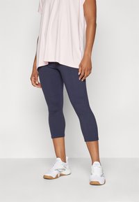 Granatowe legginsy capri wykonane z elastycznego materiału, zestawione z luźnym jasnoróżowym topem i białymi butami sportowymi z jasnobrązową podeszwą.