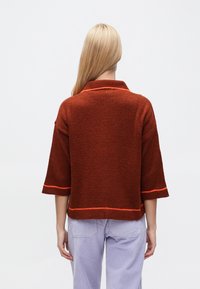 Roostevärvi kudumiga kampsun krae ja lühikeste varrukatega; ääri ääristatud kontrastse oranži õmblusega. Kandmiseks heledate pükste kohal.