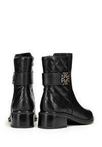 Botines negros hasta el tobillo con un diseño de cuero acolchado, puntera redonda y un tacón grueso. Presentan un emblema metálico decorativo en la correa del tobillo.