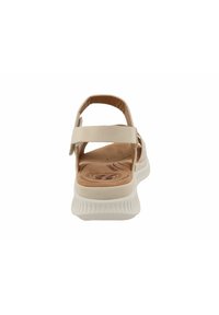 Beige sandal with a textured insole, two adjustable straps, and a white rubber outsole featuring a wave pattern for grip.