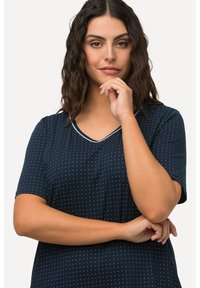 Námorníckomodré tričko s krátkymi rukávmi s bielymi bodkami, v výstrihu do V a kontrastným lemovaním. Hladká tkanina s voľným strihom.