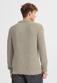 Light grey knit sweater with a textured finish, ribbed cuffs, and a collar. Features a slightly elongated back hem and fitted design.