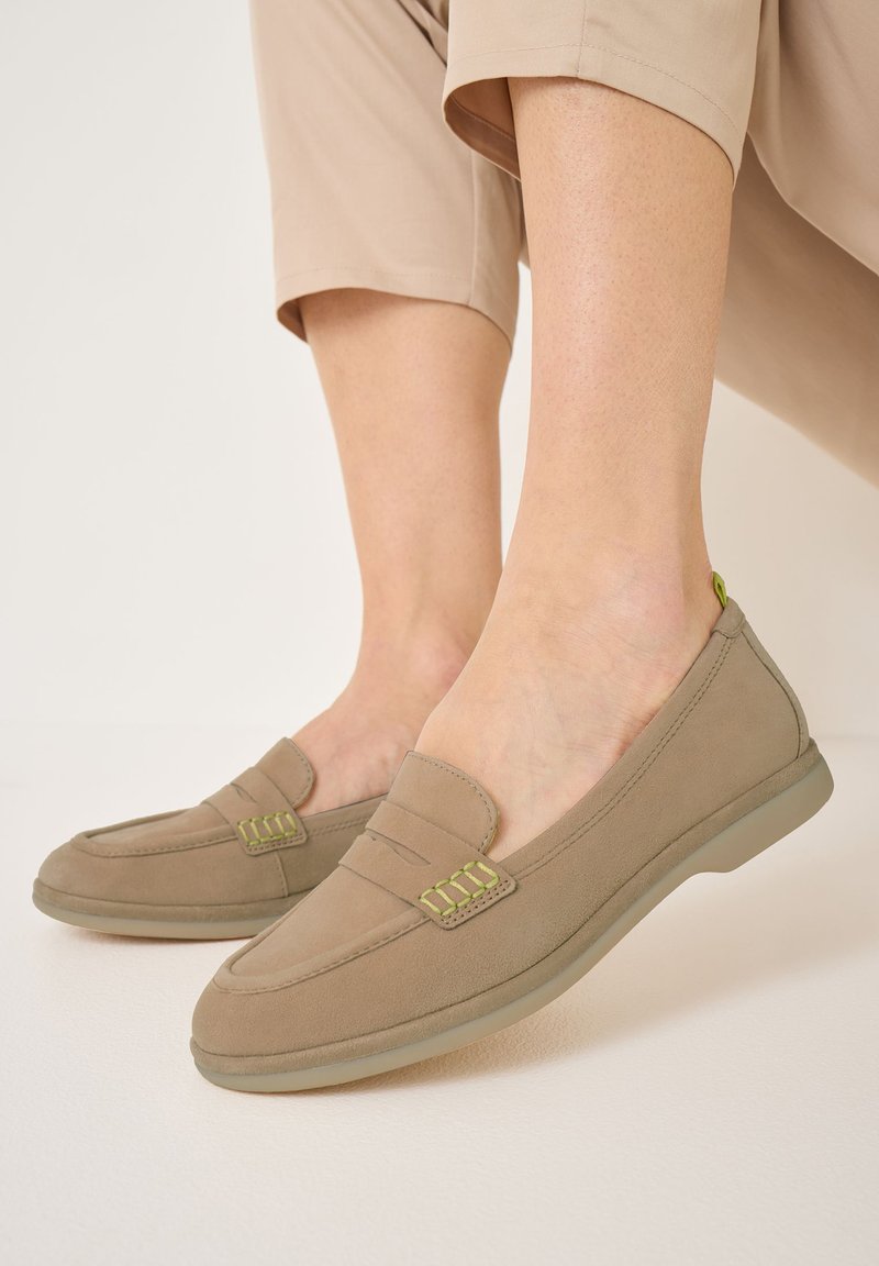 Béžové slip-on boty s hladkým semišovým povrchem, se zelenými švy a zaoblenou špičkou. Podešev je flexibilní a polstrovaná.