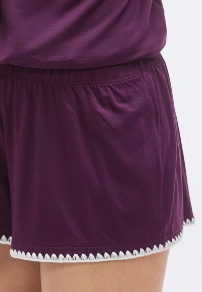 Lila pamut rövidnadrág elasztikus derékpánttal és fehér hullámos szegéllyel. Oldalzsebekkel és laza szabással rendelkezik.