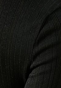 Černá ripová látka s jemnými stříbrnými glitry, s vertikálními pruhy, které vytvářejí texturovaný vzhled.
