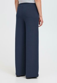 Navy wide-leg trousers with a smooth, stretchy fabric, featuring a high waistband and side pockets, worn with a gray top.