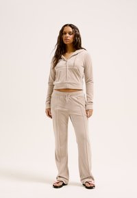 Tan velours trainingspak met een cropped zip-up hoodie en rechte broek, aangevuld met subtiele stiksels en trekkoorddetails.